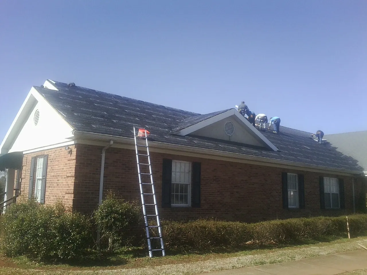 Crew tearing shingles off a brick ranch roof with a ladder set — Emergency Roof Repair work by our crew in Dougherty