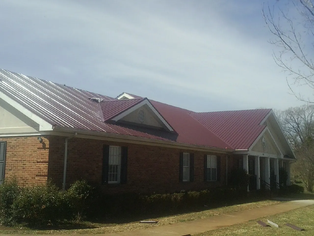 Red metal roof with gabled entries on a long brick building, from a Hail Damage Roof Repair job in Dougherty